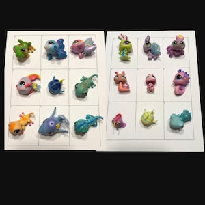 May include: A collection of colorful, small plastic animal figurines, including fish, frogs, and other creatures. The toys are arranged in a grid pattern on a white background. The figurines are in various colors, such as green, blue, pink, and yellow.