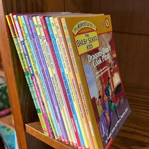 Puede incluir: Una estantería con una colección de 18 libros de bolsillo de colores. Los libros se titulan "The Bailey School Kids" y presentan varios títulos como "Dragons Don't Cook Pizza", "Gremlins Don't Chew Bubble Gum" y "Hercules Doesn't Pull Teeth".