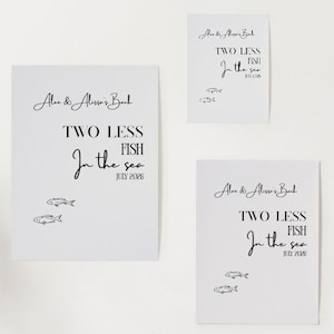 May include: A modern interior scene featuring two green velvet chairs, a small black side table with a green lamp, and three framed prints on a white wall. The prints display the text "Two Less Fish in the Sea."