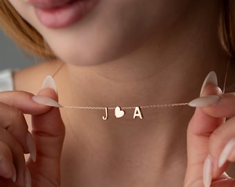 May include: A delicate gold necklace with a heart charm and two initial charms, J and A.
