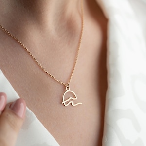 May include: A gold necklace with a delicate pendant featuring a stylized sun and wave design.