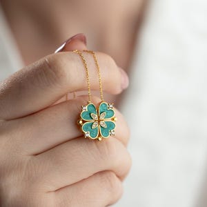 Könnte beinhalten: Eine goldene Halskette mit einem vierblättrigen Kleeblatt-Anhänger. Das Kleeblatt ist aus Gold gefertigt und hat eine grüne Emaille-Mitte mit kleinen, klaren Steinen.