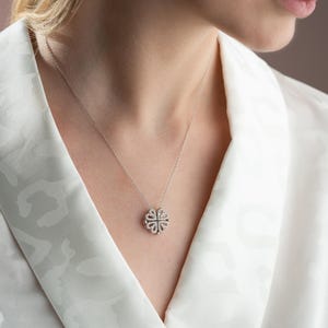 May include: A silver necklace with a delicate, diamond-shaped pendant. The pendant is made up of smaller diamonds arranged in a floral pattern.