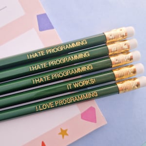 May include: Five green pencils with gold lettering. The pencils have the following text: "I hate programming", "I hate programming", "I hate programming", "It works!" and "I love programming".