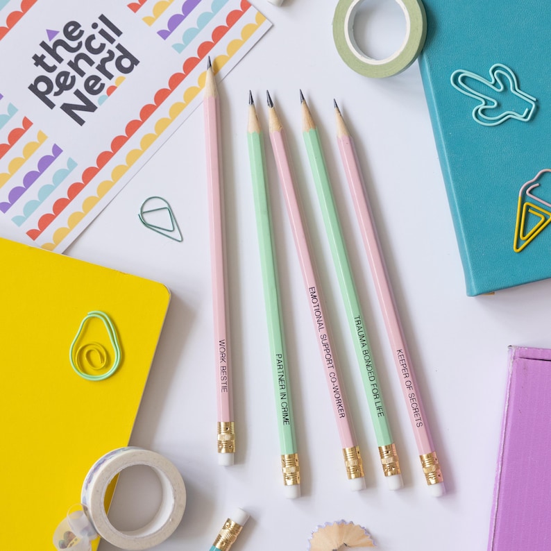 May include: Four pencils with different colored bodies and eraser tops. Each pencil has a different funny saying written on it in black text. The sayings are "Keeper of Secrets", "Trauma Bonded for Life", "Emotional Support Co-worker", "Partner in Crime", and "Work Bestie".