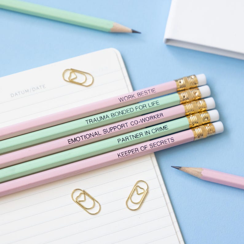 May include: Five pencils with different colored stripes and funny friendship titles printed on them. The titles are "Work Bestie", "Trauma Bonded for Life", "Emotional Support Co-Worker", "Partner in Crime", and "Keeper of Secrets".
