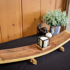 May include: A wooden serving tray made from a reclaimed wine barrel with a natural wood finish. The tray is curved and has two wooden legs. A white candle is in a black glass holder on the tray.
