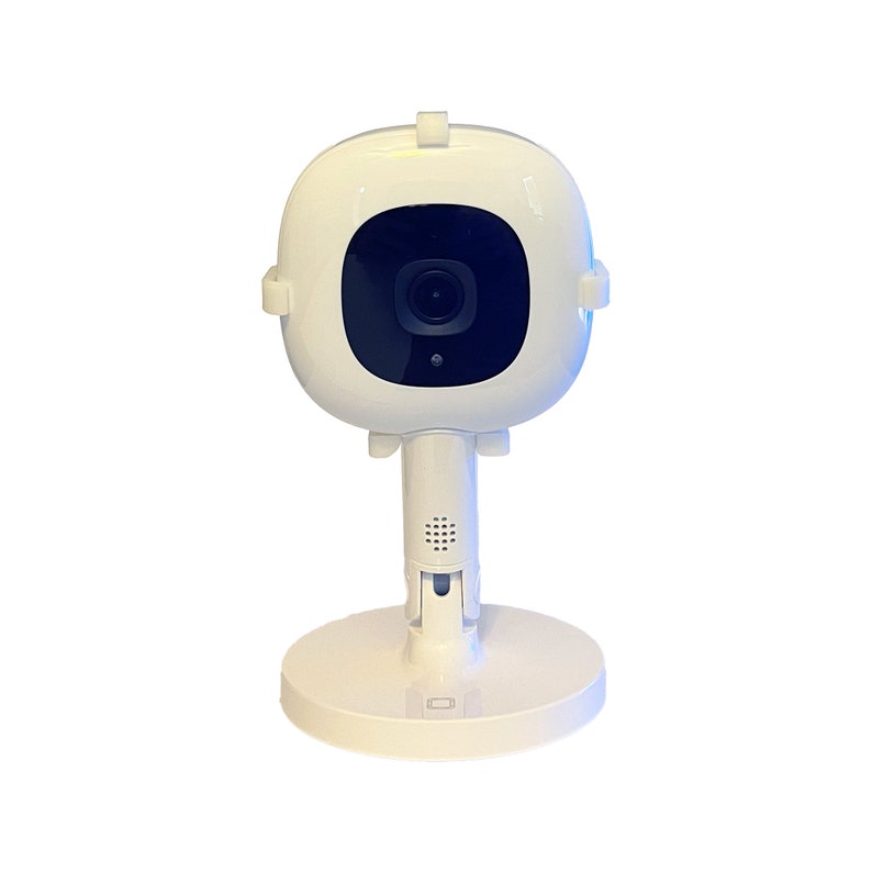 May include: A white baby monitor with a round camera lens and a stand. The camera is mounted on a swivel base.