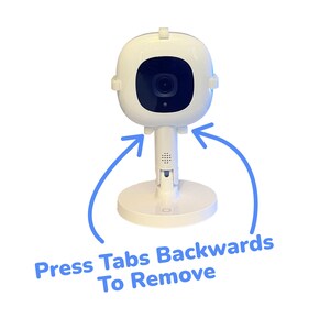 May include: White baby monitor with a round camera lens and a base. The base has two tabs on the sides that can be pressed backwards to remove the camera from the base.