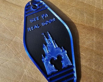 May include: Blue and black key chain with a Mickey Mouse silhouette and a silhouette of Cinderella's castle. The key chain has the text "See ya real soon".