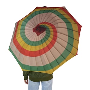 May include: A colorful umbrella with a spiral design. The umbrella features alternating bands of red, yellow, green, and beige. The umbrella is open, and the handle is not visible. The umbrella is held by a person wearing a green jacket and blue jeans.