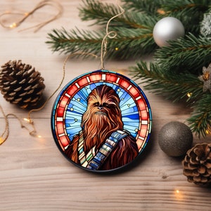 May include: A round Christmas ornament featuring a stained glass design of Chewbacca from Star Wars. The ornament is blue, red, and yellow with a black outline.