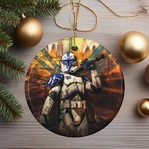 May include: A round ceramic Christmas ornament featuring a Star Wars clone trooper in blue and white armor, standing in front of a stained glass window with a sunset background.
