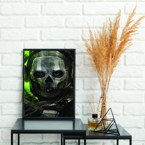 May include: Framed artwork featuring a skull with a headset, set against a green and black background. The skull has a gray and white color scheme. The artwork is displayed on a black table with decorative items.