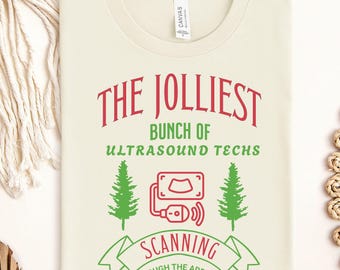 May include: A beige t-shirt with a red and green design that says "The Jolliest Bunch of Ultrasound Techs" and "Scanning Through the Add Ons & Lunch Breaks". The design features a stylized ultrasound machine and two green pine trees.