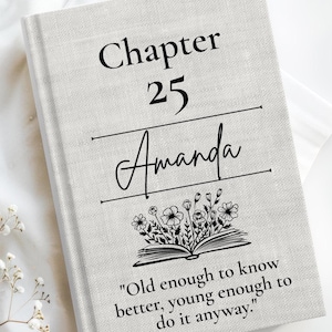 May include: A light gray, textured hardcover book with black text that reads Chapter 25 Amanda, followed by a line drawing of an open book with flowers growing out of it, and the quote Old enough to know better, young enough to do it anyway.
