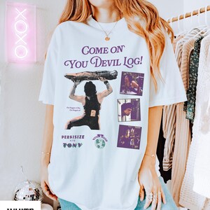May include: White t-shirt with a graphic design featuring the text "Come On You Devil Log!" in purple, along with an illustration of a person holding a log and three smaller images. The shirt also includes the text "Perkisize with Tony".