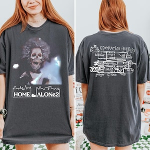 May include: Dark gray t-shirt featuring a graphic of a skeleton with a fuzzy afro and the text "HOME ALONE 2". The back of the shirt has a schematic drawing with the text "OPERATION HOHOHO" and "garbage by Kevin 'hole'".