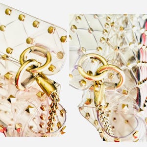 May include: Clear, geometric-patterned handbag with gold-tone hardware. The bag features a chain strap and is adorned with gold studs. The clasp and chain are also gold, creating a cohesive and stylish accessory.