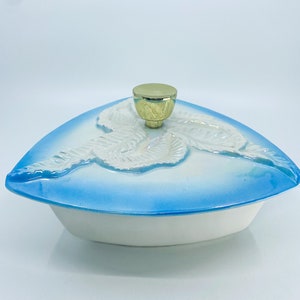 May include: A white and blue ceramic serving dish with a lid. The lid is triangular with a gold knob and embossed white leaf design. The dish has a white base and a blue rim.