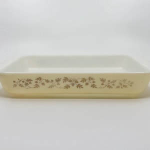 May include: A rectangular, off-white baking dish with a decorative brown floral pattern along the sides. The dish has a slightly flared rim and handles. The overall design is simple and classic, suitable for baking and serving.