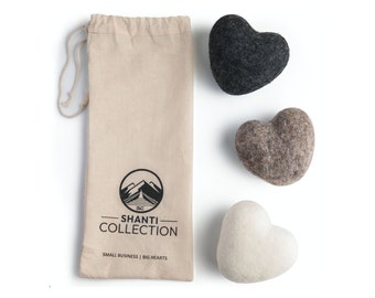 May include: Three felt heart-shaped stones in a beige drawstring bag. The bag has the text "Shanti Collection" and "Small Business | Big Hearts". The stones are black, brown, and white.