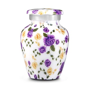 May include: A white urn with a floral design featuring purple and yellow roses. The urn has a silver band around the neck and a matching lid. The floral pattern covers the entire surface of the urn.