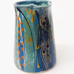 A midnight blue jug is shown on a white background. The primary colour is blue with a turquiose oval and trailed lines in bright orange, yellow, white and black. The image shows the middle of the jug, the lip is pointing to the right.