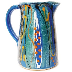 Könnte beinhalten: Eine blaue Keramikkanne mit einem weißen Henkel. Die Kanne hat ein farbenfrohes abstraktes Design mit orangefarbenen, gelben und schwarzen Akzenten.