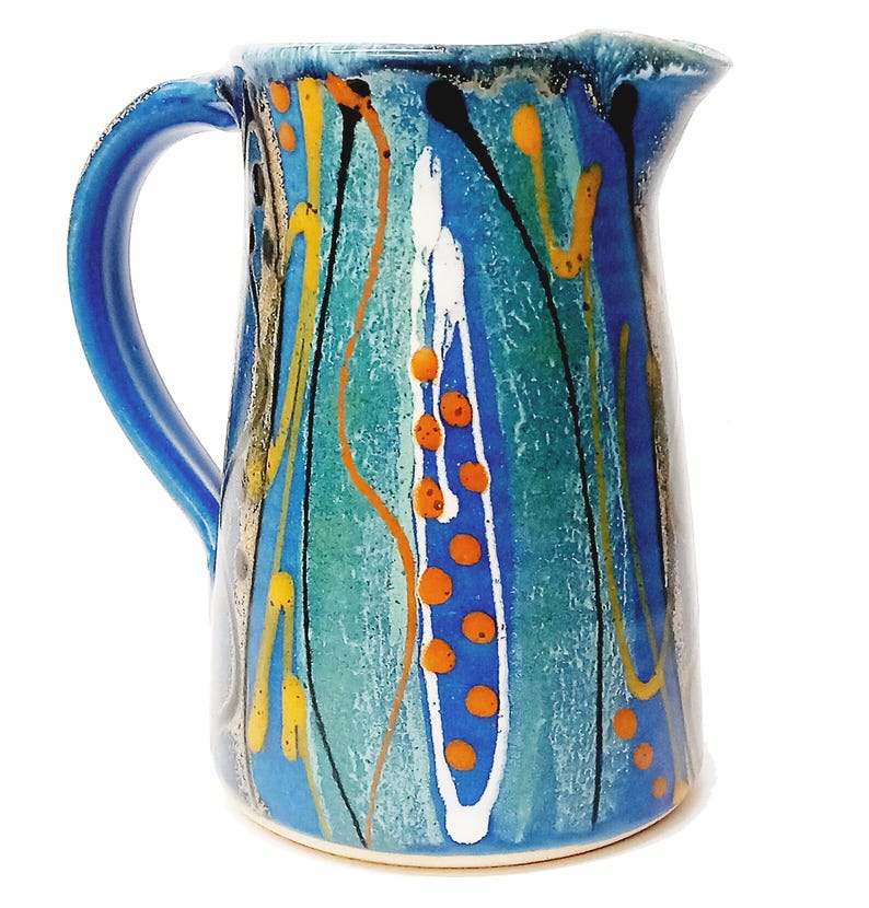 A midnight blue jug is shown on a white background. The primary colour is blue with a turquiose oval and trailed lines in bright orange, yellow, white and black. The handle points to the left.