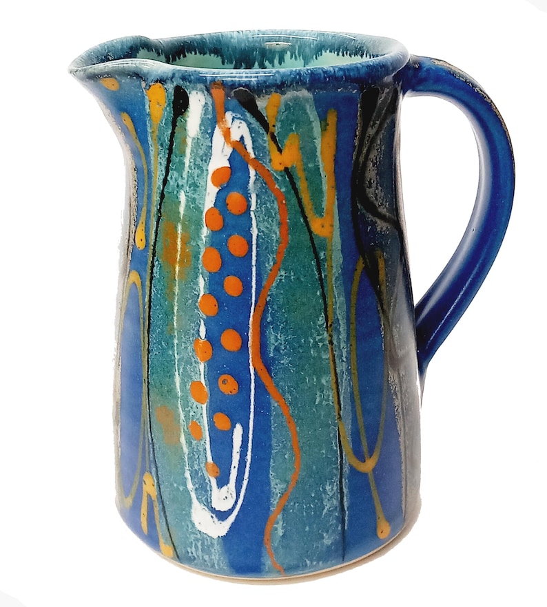A midnight blue jug is shown on a white background. The primary colour is blue with a turquiose oval and trailed lines in bright orange, yellow, white and black. The handle points to the right.