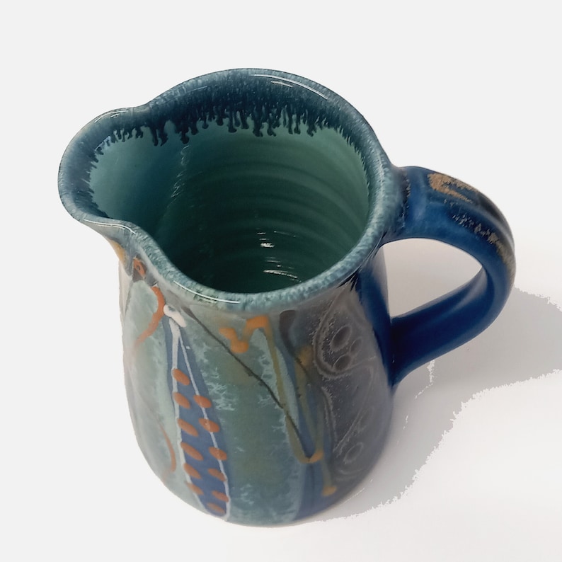 Looking down into the jug showing the interior glossy turquoise glaze. The lip is shown from above, pointing to the left, the handle is on the right.