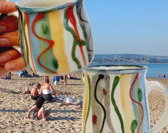 Hand made stoneware pottery mug with unique striped decoration. Vibrant colourful hand painted decoration on soft white background.