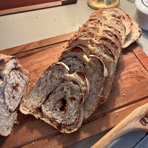 May include: A loaf of cinnamon swirl bread sliced on a wooden cutting board. The bread is light brown with a swirl of cinnamon throughout. The cutting board is made of wood and has a natural finish.