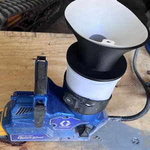May include: A blue and yellow Graco Ultimate QuickShot paint sprayer with a black and white funnel attachment. The sprayer has a black handle and a black hose. The sprayer is on a wooden surface.