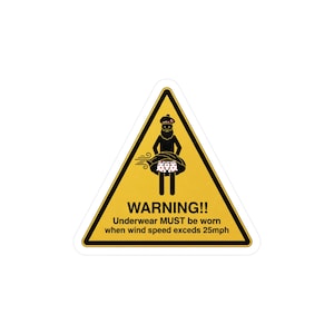 May include: A yellow triangular sticker with a black border and a warning message. The sticker features a cartoon figure wearing a crown and underwear, with the text "WARNING!! Underwear MUST be worn when wind speed exceeds 25mph."
