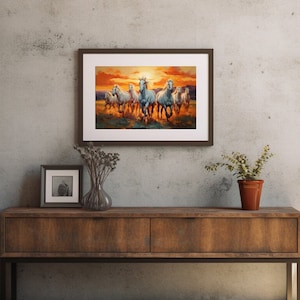 May include: A framed painting of a group of white horses running through a field at sunset. The horses are in a line, with the lead horse facing the viewer. The background is a blurry landscape with a bright orange sunset.