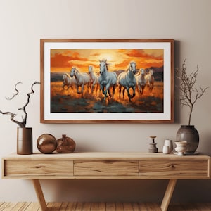May include: A framed painting of a herd of white horses running through a field at sunset. The horses are in a line, with the lead horse facing the viewer. The sky is a vibrant orange and yellow, and the field is a soft green.