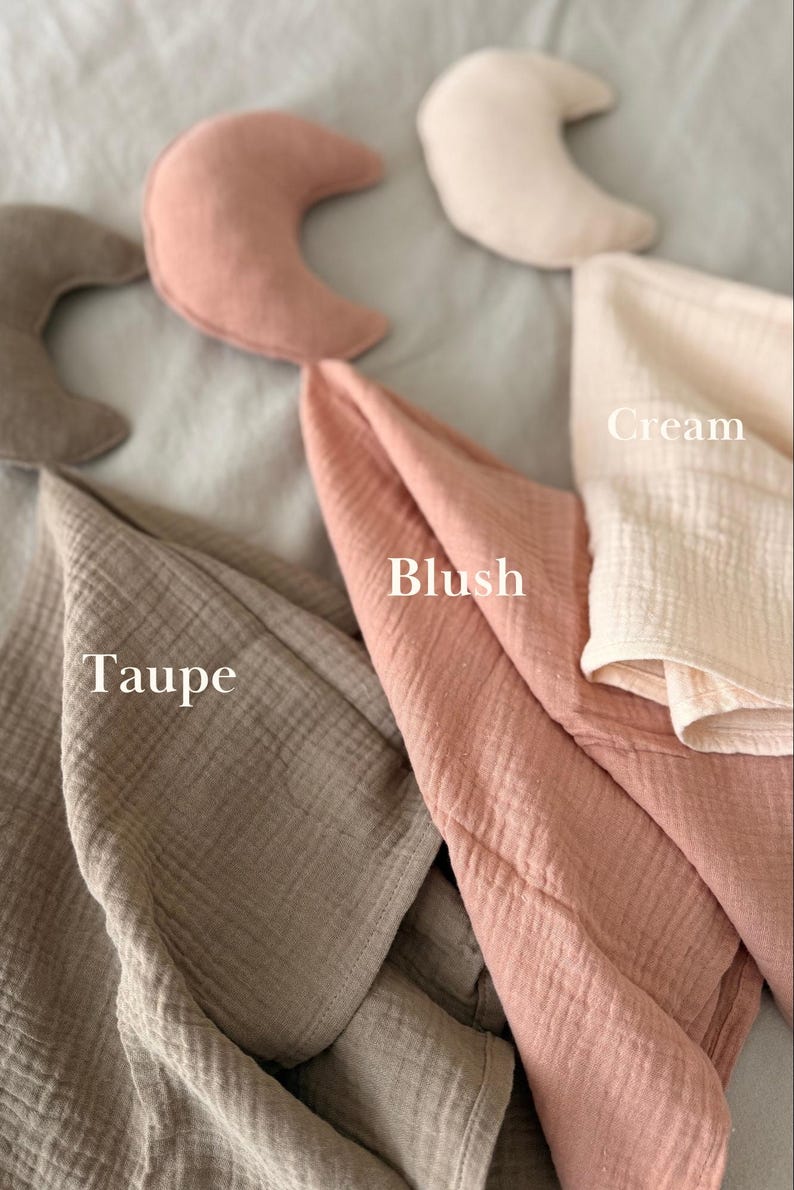 May include: A collection of crescent moon-shaped pillows and folded muslin fabric pieces in cream, blush, and taupe colors. The text labels Cream, Blush, and Taupe are printed on the image to identify the specific color of each fabric item.