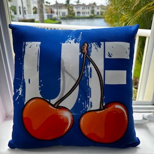 May include: Blue throw pillow with a white "UF" design and two red cherries.