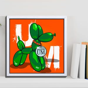 Puede incluir: Una impresión enmarcada con una ilustración de perro globo verde sobre un fondo naranja. El perro tiene una etiqueta que dice "return to: UM". Letras y salpicaduras blancas también están en el fondo naranja.