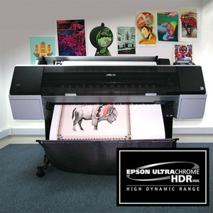 May include: A black and silver Epson printer with a large format print of a buffalo with a headdress coming out of the printer. The printer is on a gray carpet and the text "EPSON ULTRACHROME HDRINK HIGH DYNAMIC RANGE" is on a black oval sticker in the lower right corner of the image.