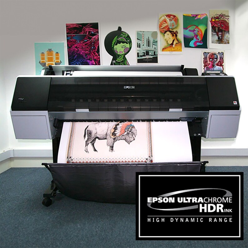May include: A black and silver Epson printer with a large format print of a buffalo with a headdress coming out of the printer. The printer is on a gray carpet and the text "EPSON ULTRACHROME HDRINK HIGH DYNAMIC RANGE" is on a black oval sticker in the lower right corner of the image.