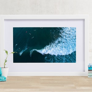 May include: An aerial photograph of a wave breaking in the ocean. The wave is white and foamy, and the water is a deep blue. There are several surfers in the water, riding the wave.