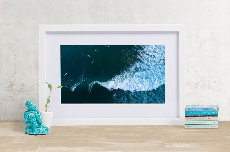 May include: An aerial photograph of a wave breaking in the ocean. The wave is white and foamy, and the water is a deep blue. There are several surfers in the water, riding the wave.