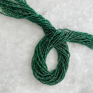 May include: A strand of dark green faceted beads. The beads are small and round, and they are strung together on a clear thread.