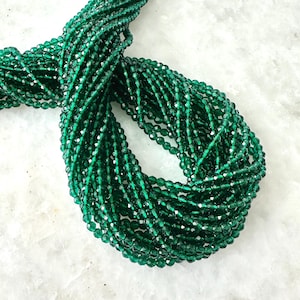 May include: A strand of emerald green faceted glass beads. The beads are small and uniform in size, and they are strung together on a clear thread.