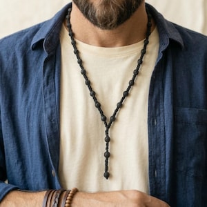 Könnte beinhalten: Eine weiße Keramiktasse mit schwarzem Henkel und dem Text "But First, Coffee" in fetter, schwarzer Schrift. Die Tasse steht vor einem verschwommenen Hintergrund, der eine gemütliche Umgebung suggeriert.