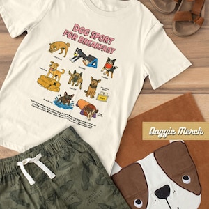 May include: A cream-colored t-shirt with the text "DOG SPORT FOR BREAKFAST" and illustrations of dogs participating in various activities. Also, green shorts with a crocodile pattern and a dog-themed pillow are visible.