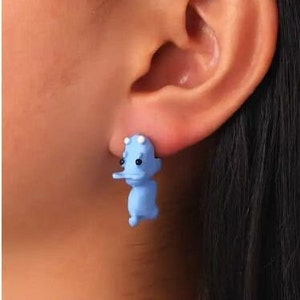 May include: A pair of blue hippopotamus stud earrings. The earrings are made of a smooth, plastic-like material and have a 3D design.
